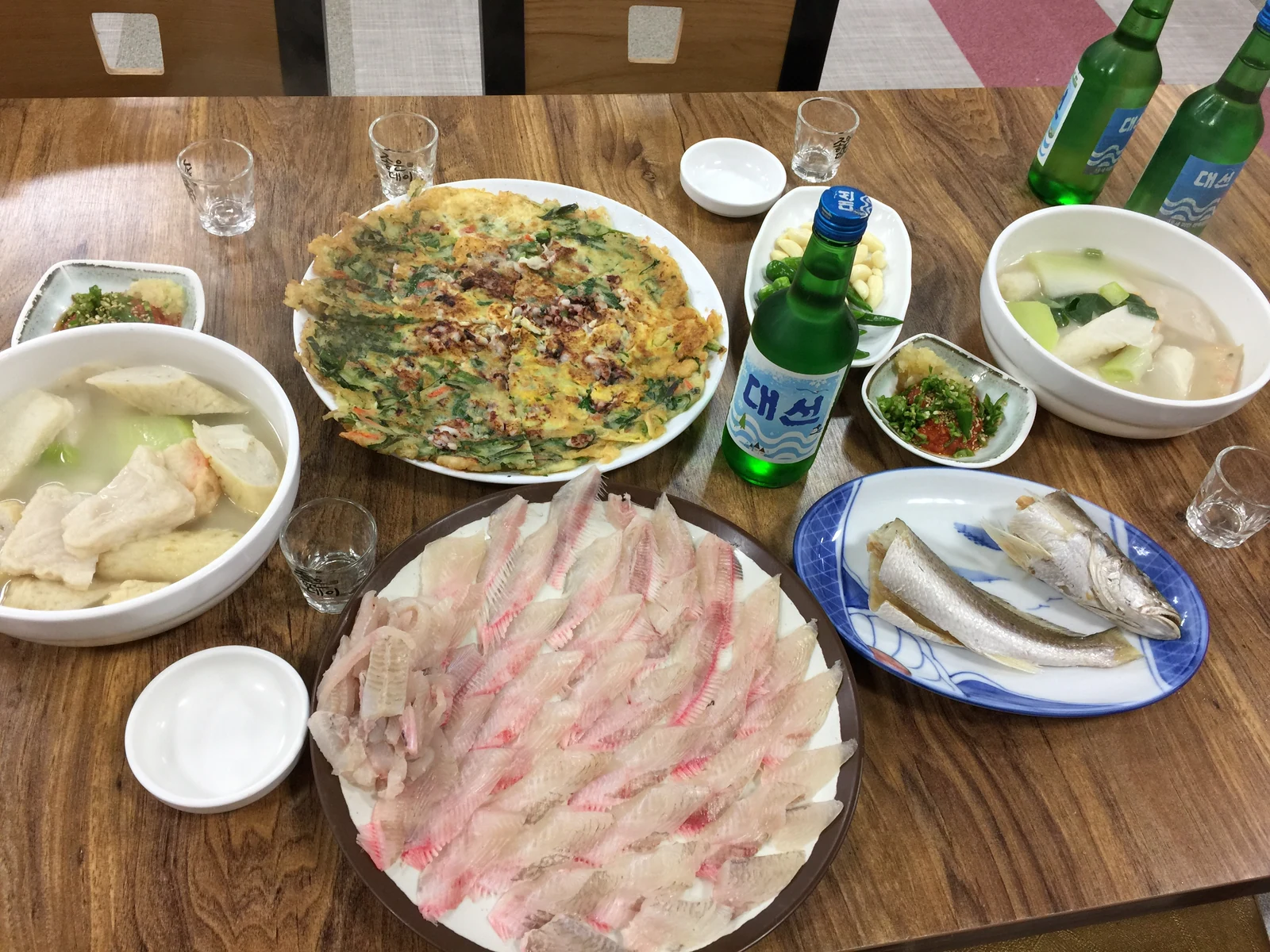 나무 상 위에 회 한 접시와 부침, 국물 요리, 구운 생선이 함께 차려진 모습.